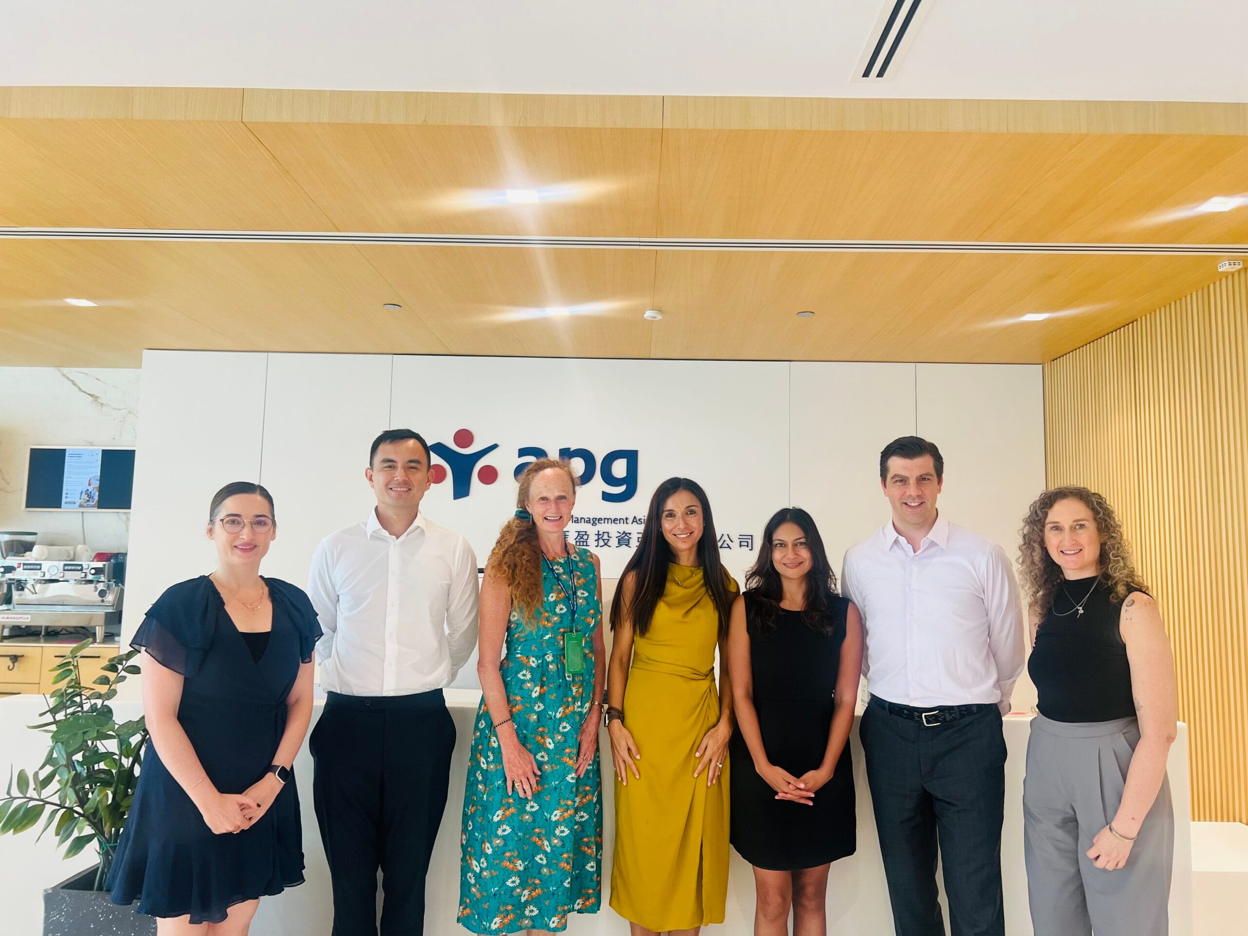 Group of men and women with business attire posing in front of an APG sign at the office